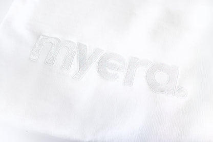 A close-up of a white textured fabric with the word 'myera.' embroidered in matching white thread. crewneck close up clothing