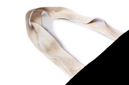 Close-up of a beige woven fabric tote bag handle, shown against a white background with a black cotton tote bag in corner. myera bag with gold ingot. printed gold and white
